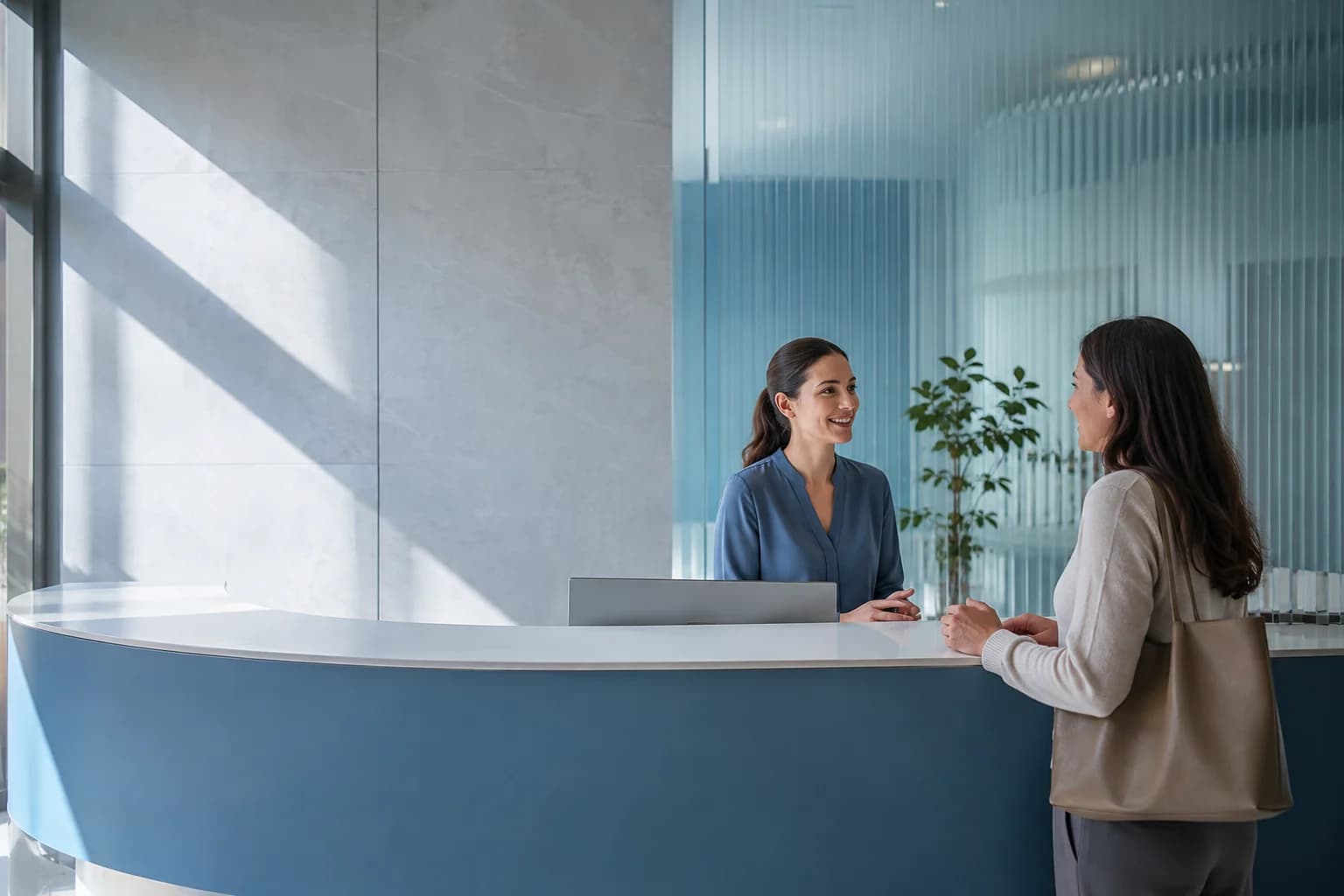 Una recepcionista atiende con calma a una visitante en una clínica luminosa. Imagen ilustrativa.